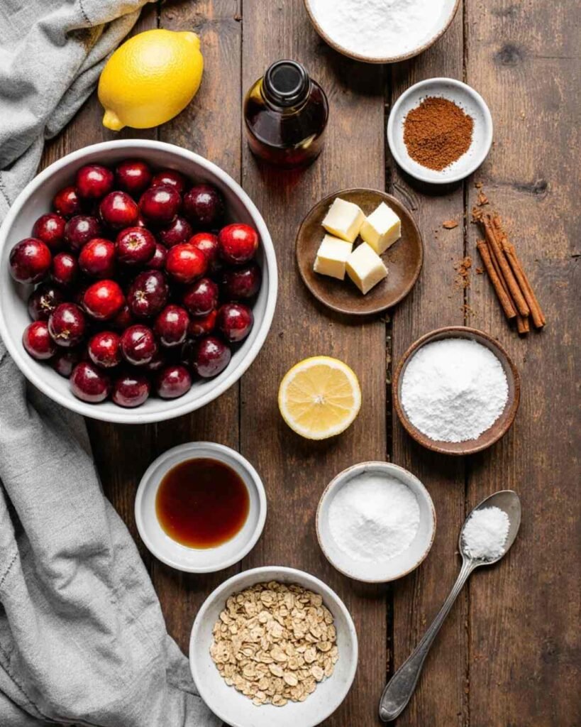 Flat lay of fresh cherries, oats, flour, sugar, butter cubes, and other ingredients for a homemade cherry crisp recipe.