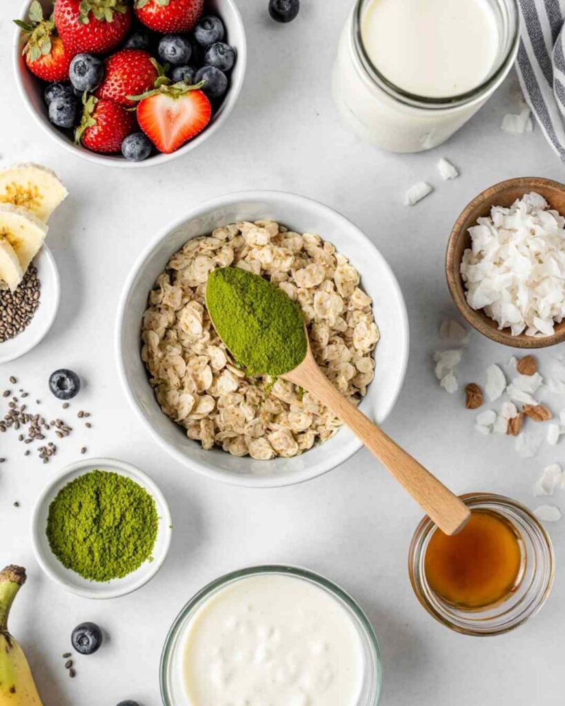 Flat-lay of ingredients for Matcha Overnight Oats Recipe: oats, matcha powder, milk, yogurt, chia seeds, honey, and fresh fruit toppings